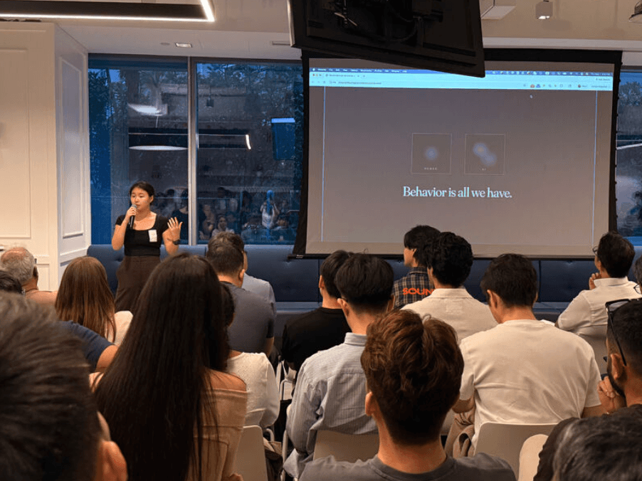Minu presenting at the AI Engineer UnConference; the slide reads: Behavior is all we have.