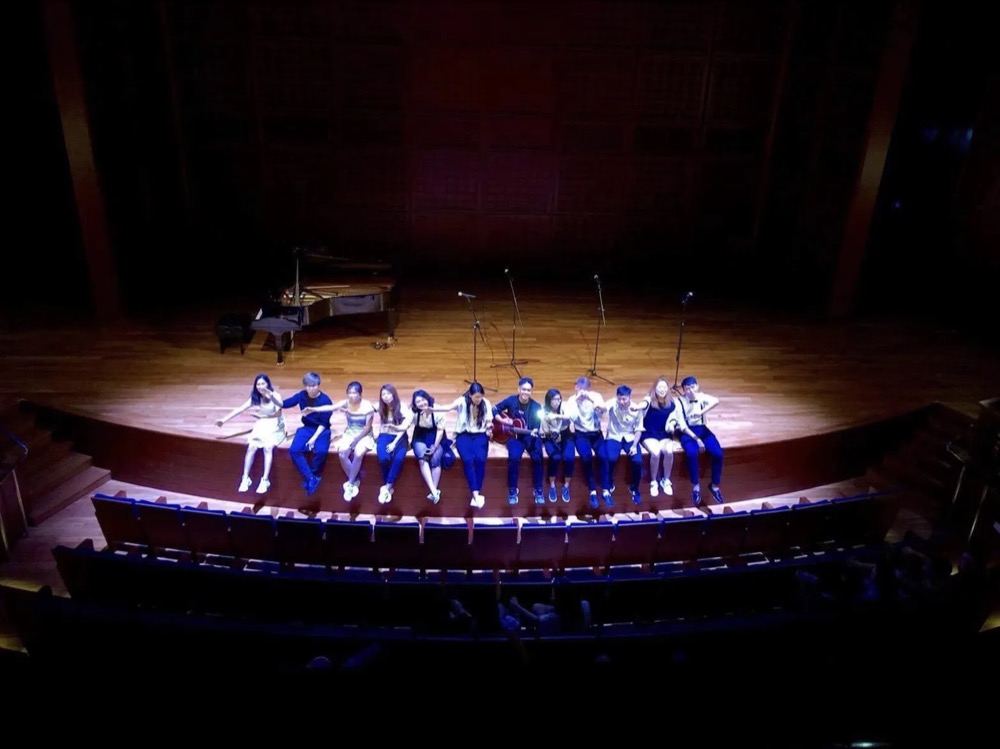 Acamando seated across the edge of a wooden concert stage
